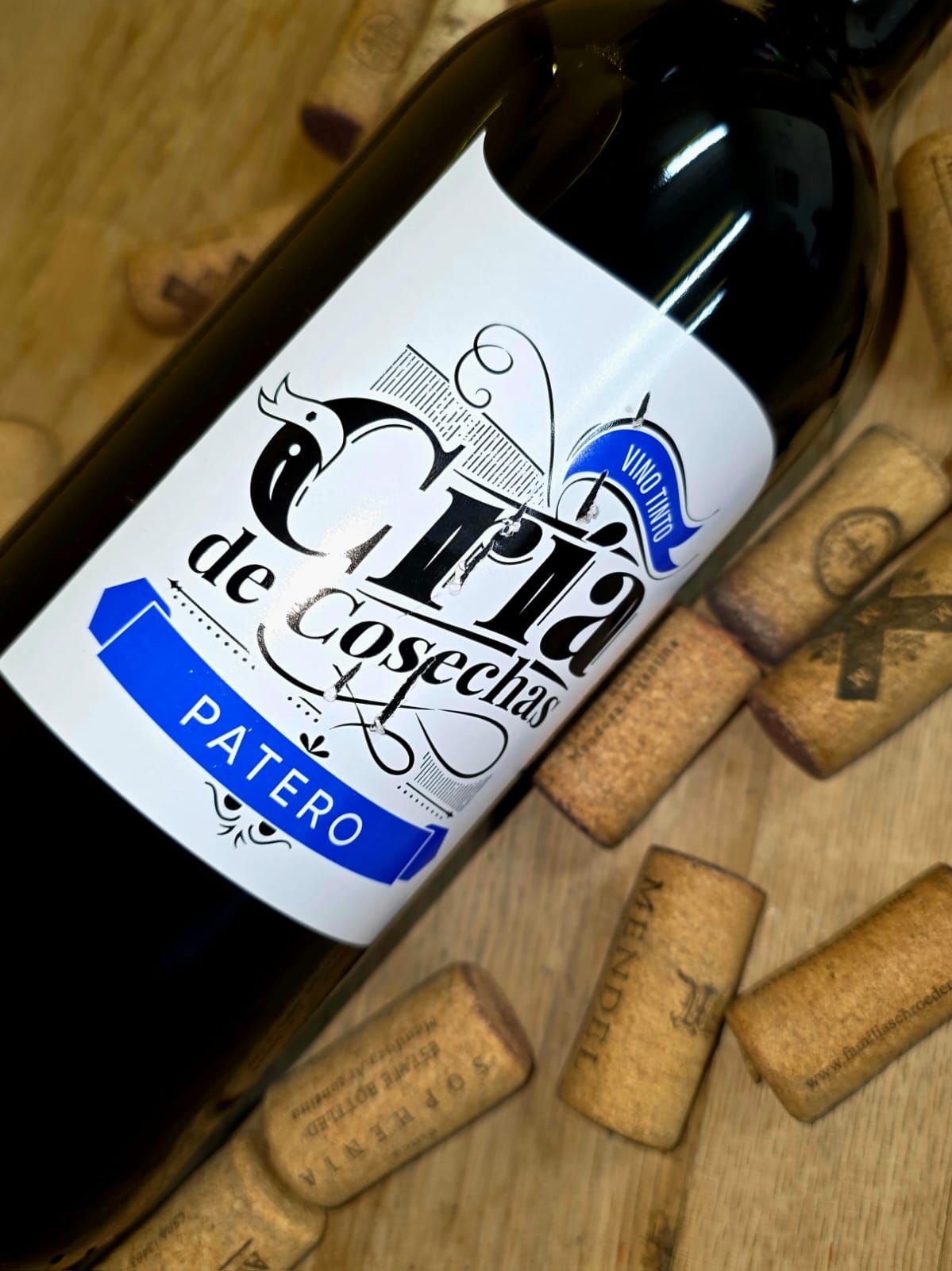 Una botella de vino Cría de Cosechas Patero sobre una superficie de madera rodeada de corchos de vino.