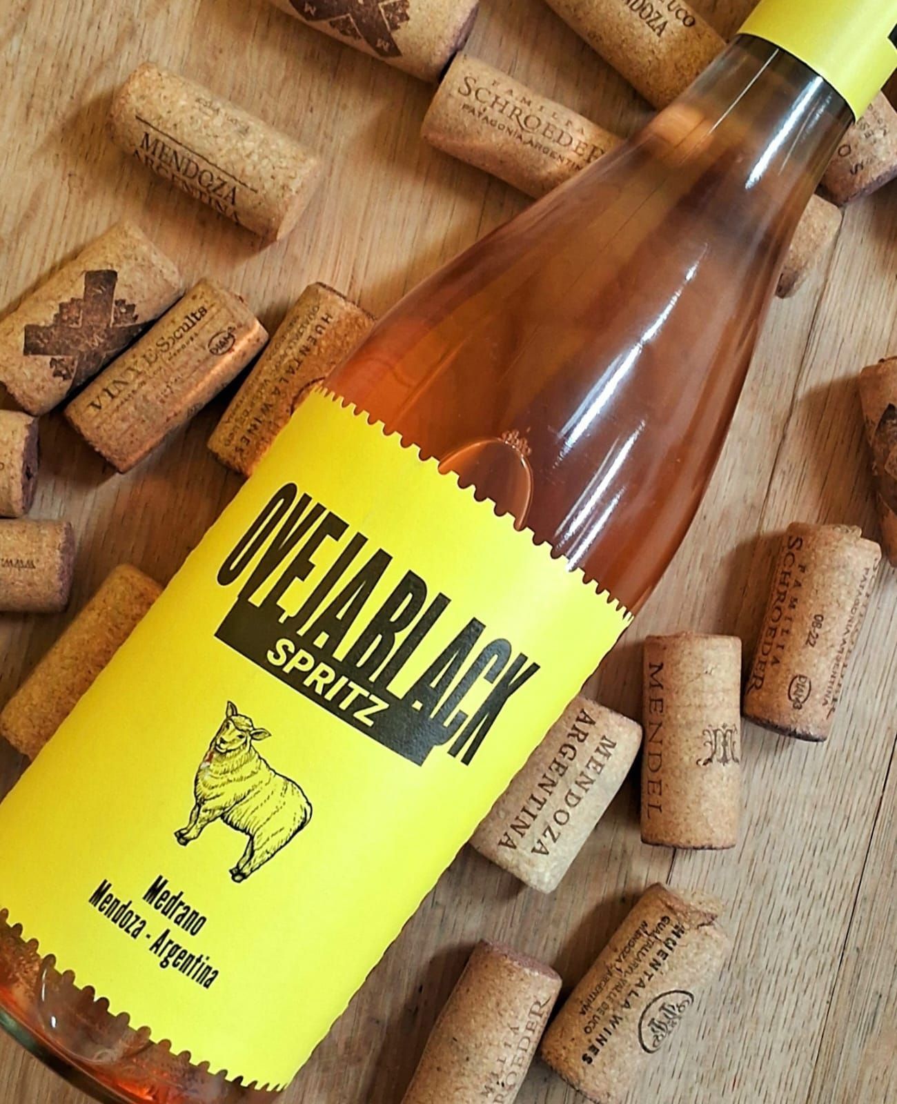 Una botella de vino OVEJA BLACK SPRITZ con una etiqueta de color amarillo brillante, rodeada de corchos