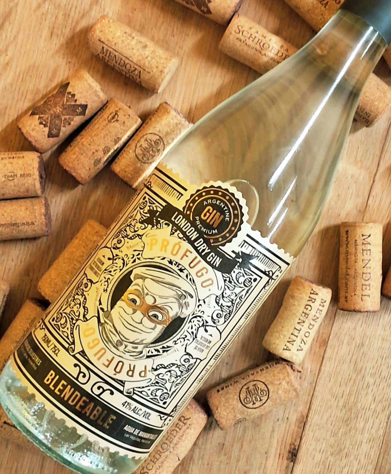 Una botella de Prófugo London Dry Gin rodeada de corchos de vino esparcidos sobre una superficie de madera clara.