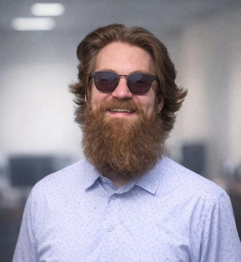 Man with red beard and gray shirt smiling, against a blue background, logo 