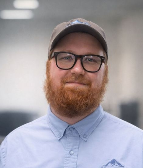 Man with red beard and gray shirt smiling, against a blue background, logo 