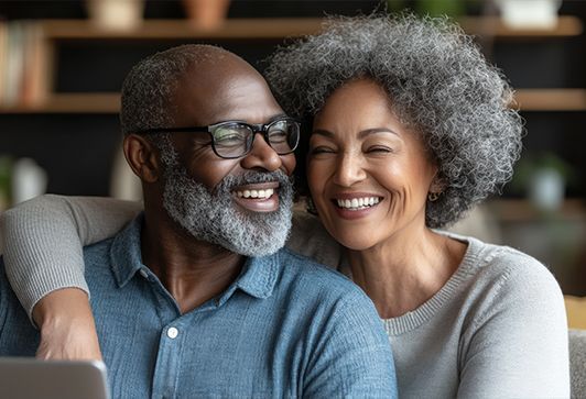 Smiling couple, embracing indoors. Man with glasses and beard, woman with curly hair.