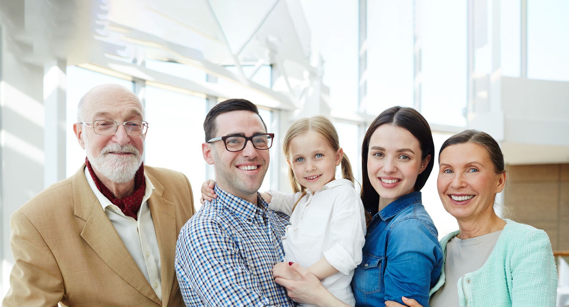 Family portrait, five people smiling inside a bright building.