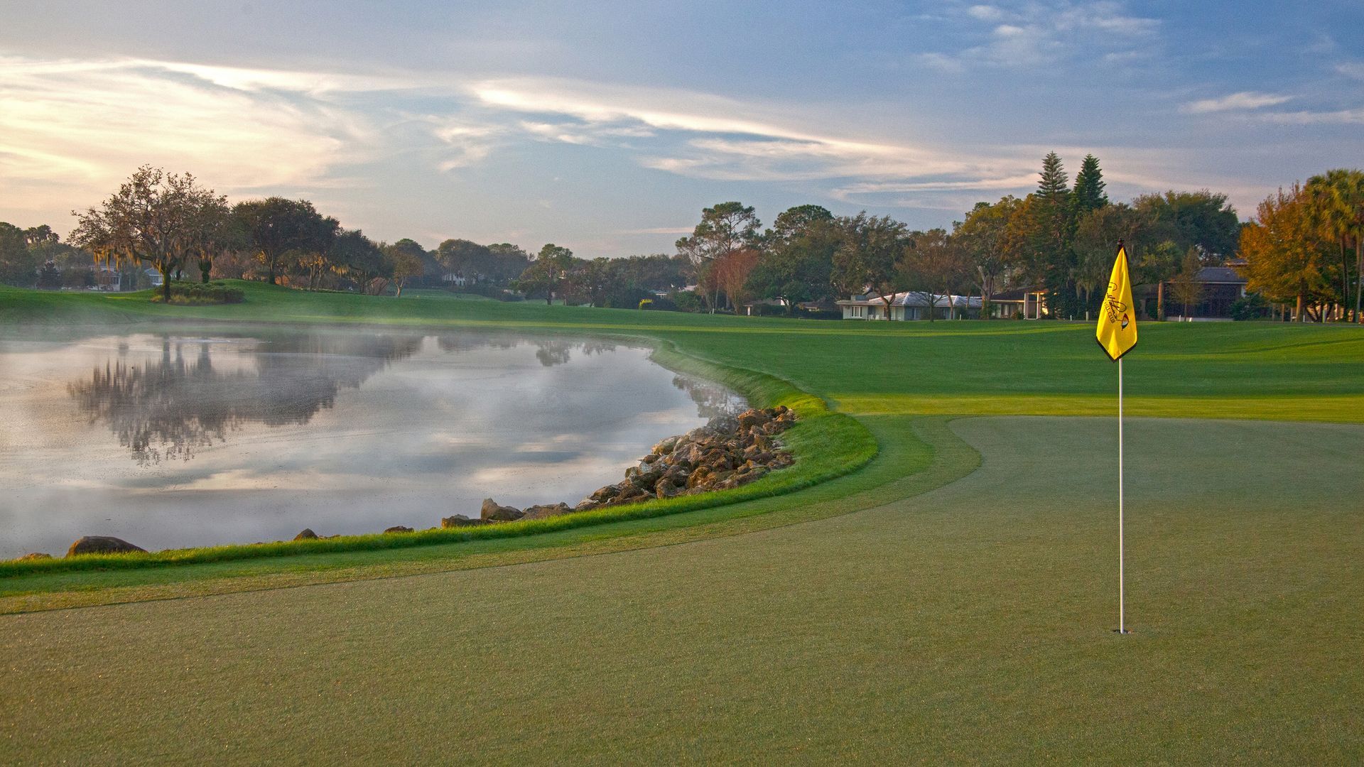 A golf course with a lake in the background and a yellow flag on the green