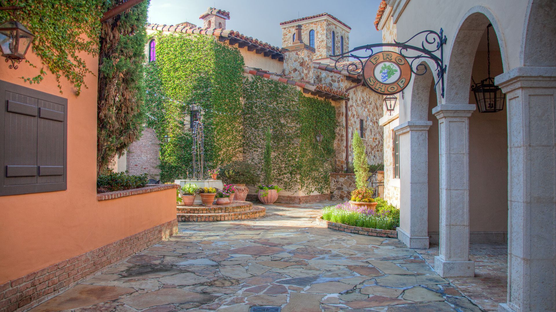 A stone walkway between two buildings with a sign hanging from the side of it.