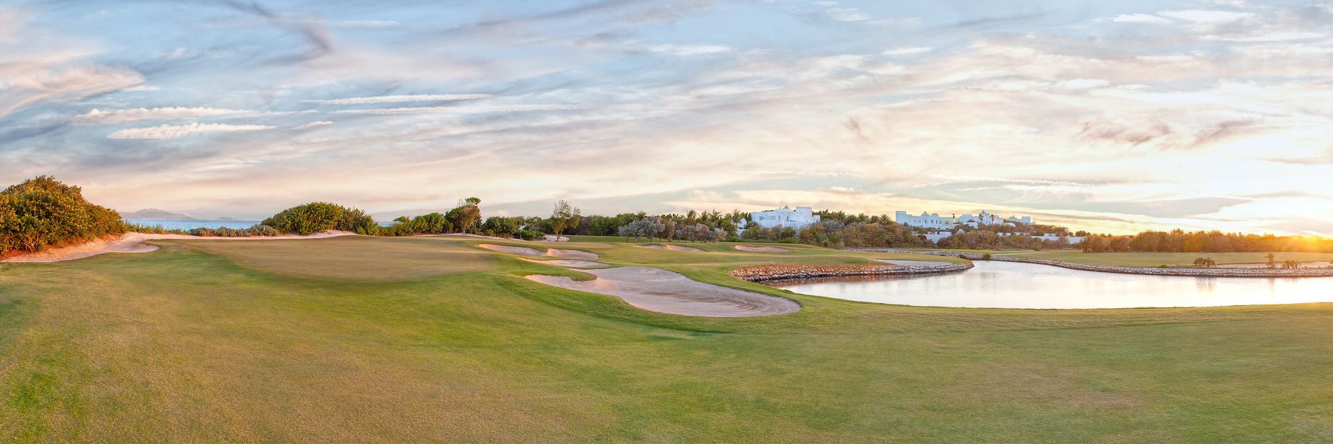 A panoramic view of a field with trees and a lake at sunset.
