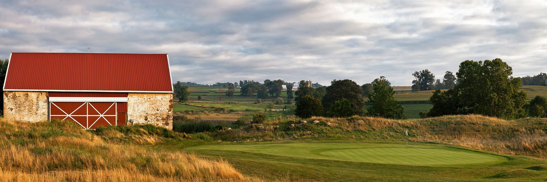 A barn with a red roof is in the middle of a field