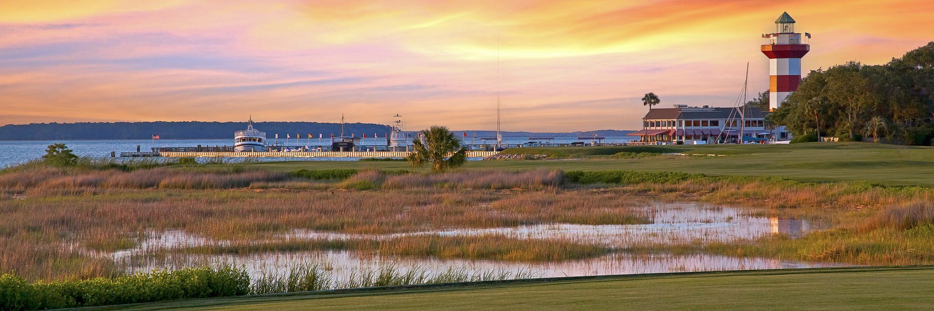 A lighthouse is sitting in the middle of a field next to a body of water.