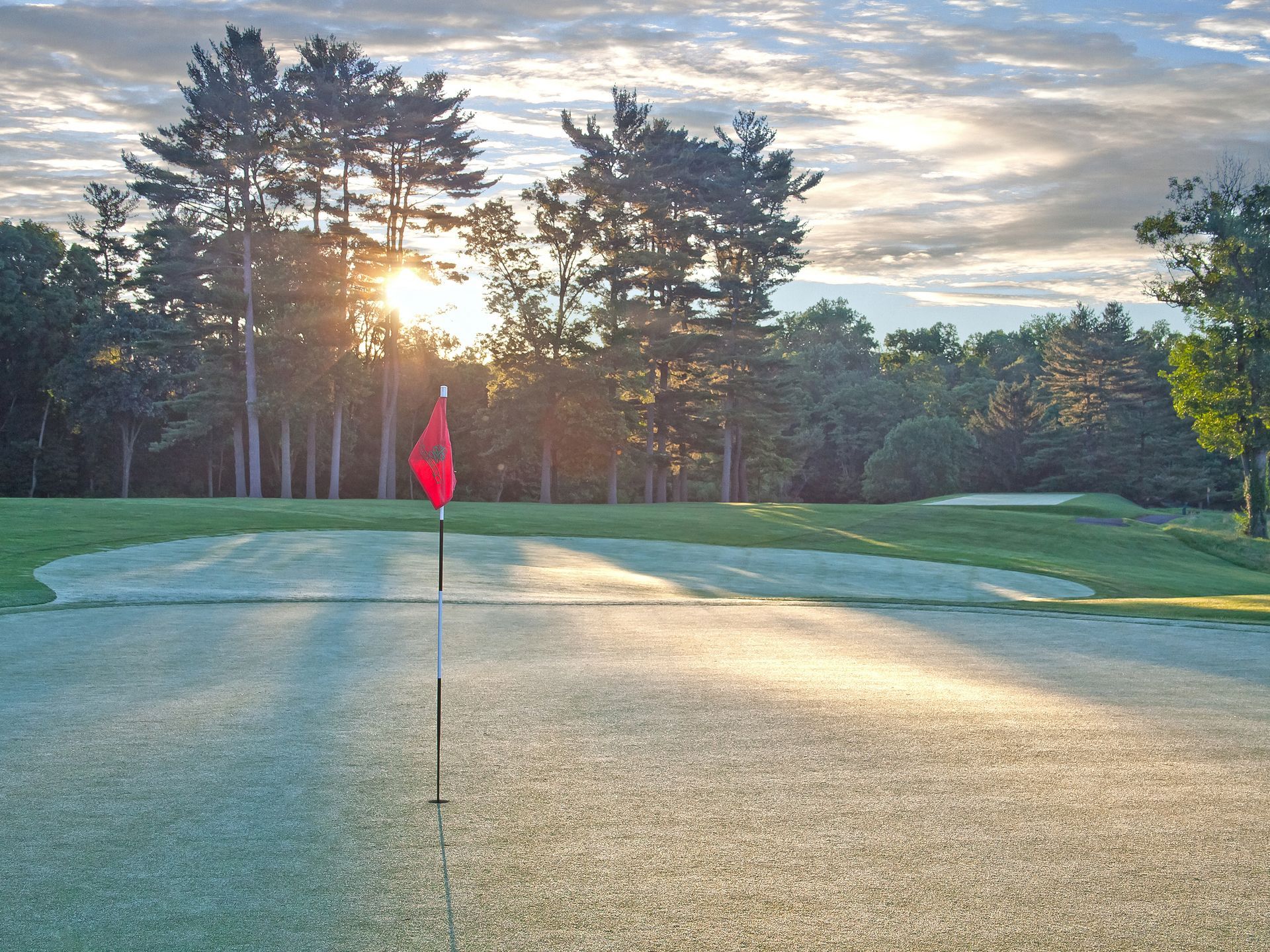 A golf course with the sun shining through the trees