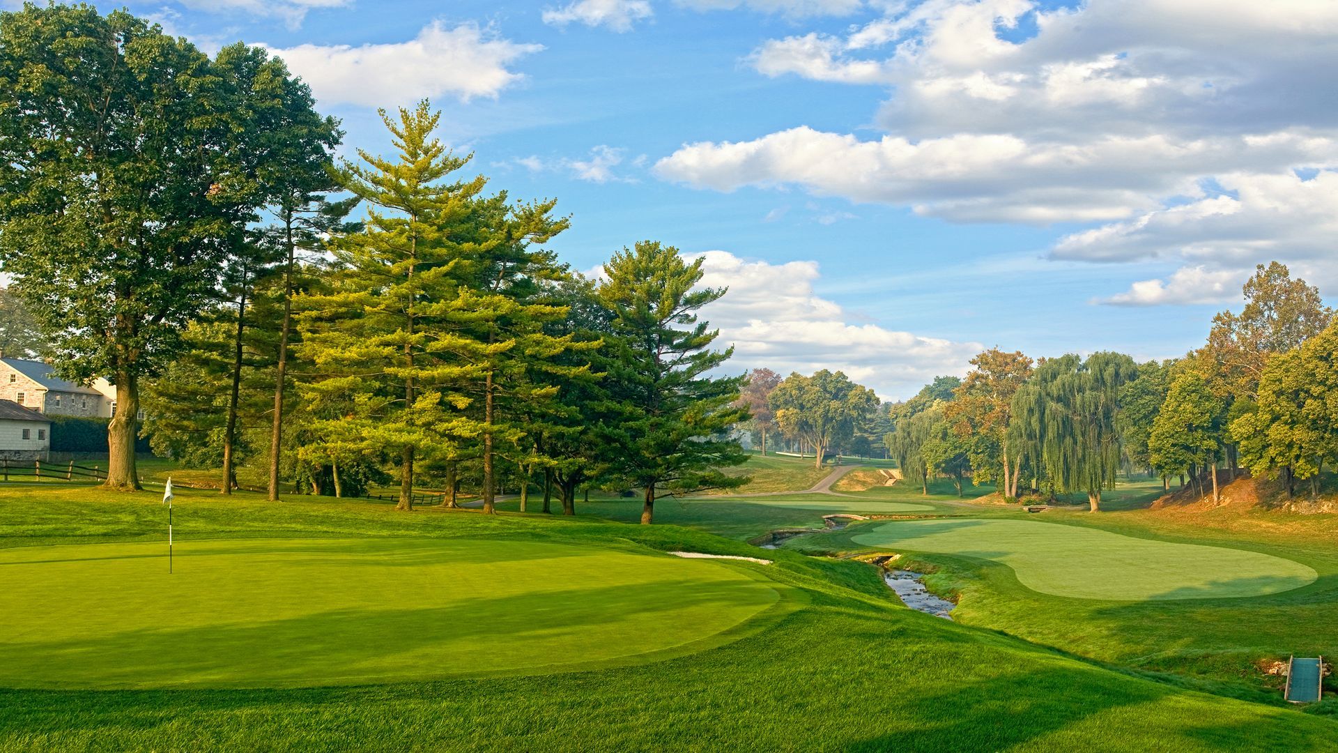 A golf course with trees and a house in the background on a sunny day.