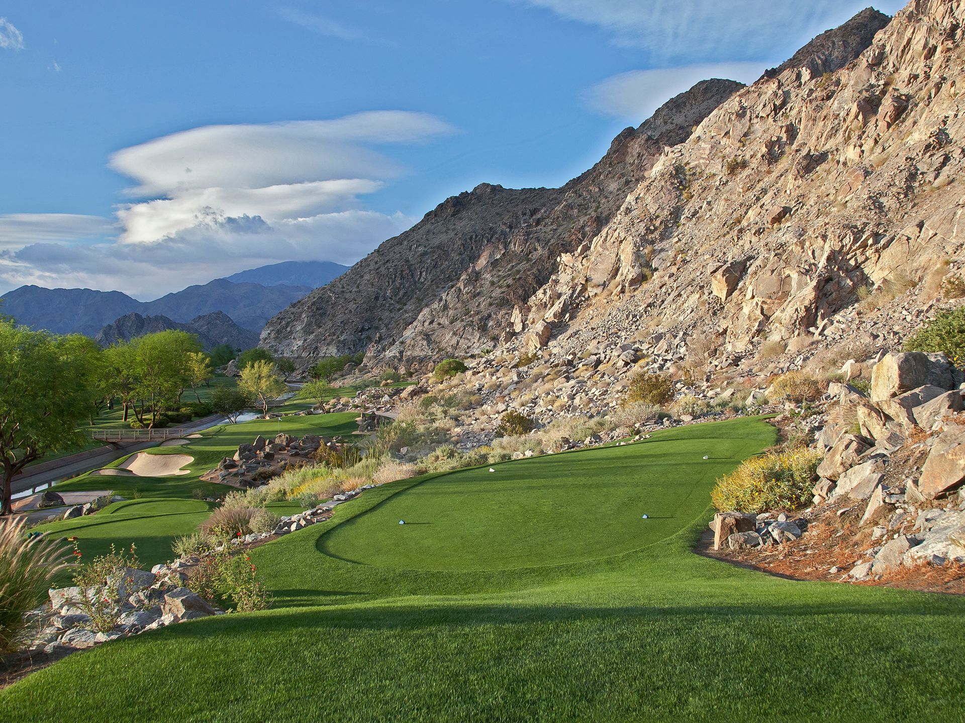 A golf course in the middle of a mountainous area with mountains in the background.