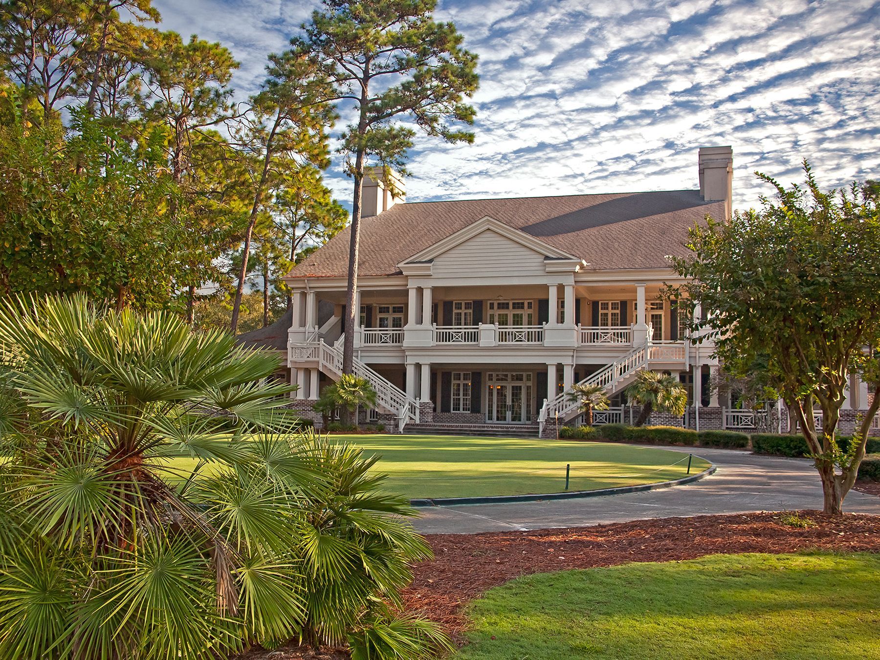 A large white house with a large lawn in front of it surrounded by trees.