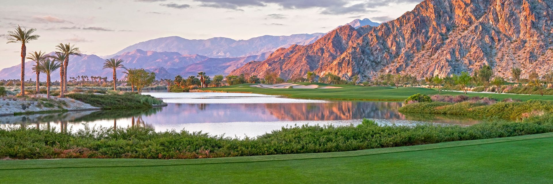 There is a lake in the middle of a field with mountains in the background.