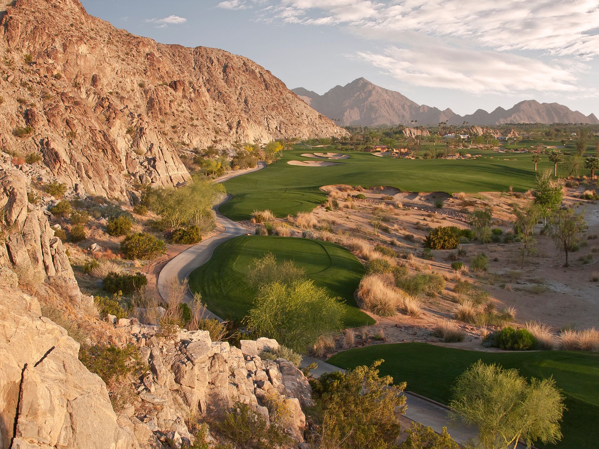 An aerial view of a golf course in the desert with mountains in the background.