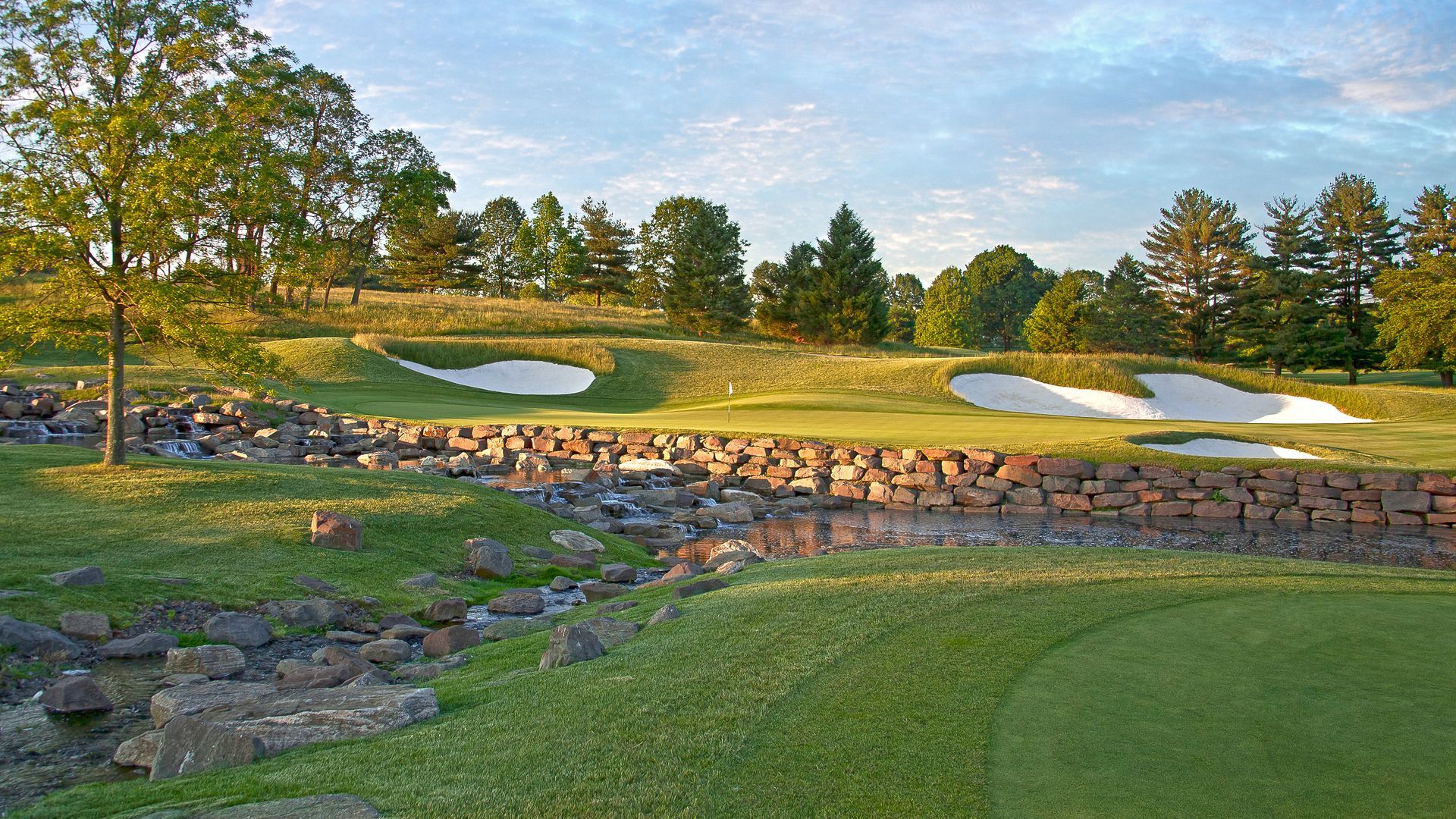 A golf course with a river running through it and trees in the background.