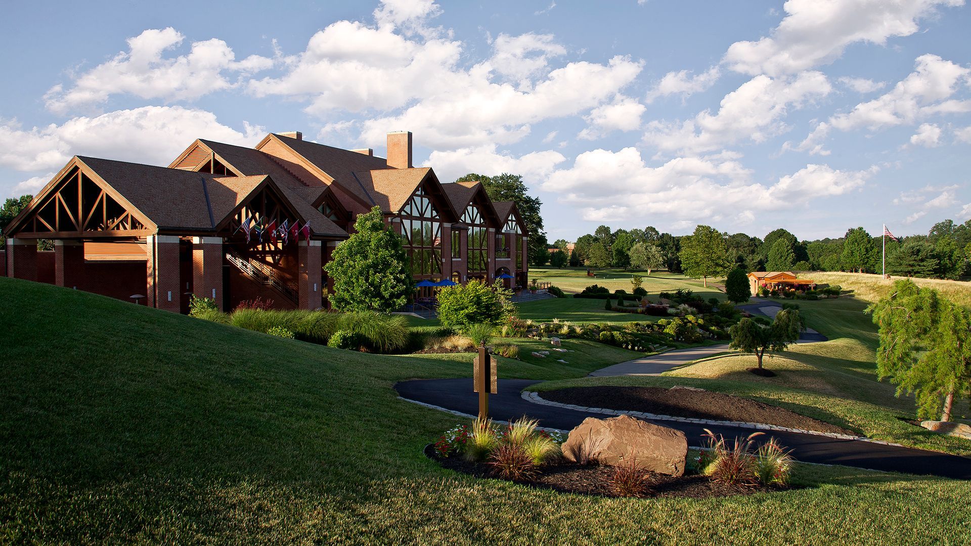 A large house is sitting on top of a lush green hill surrounded by trees.