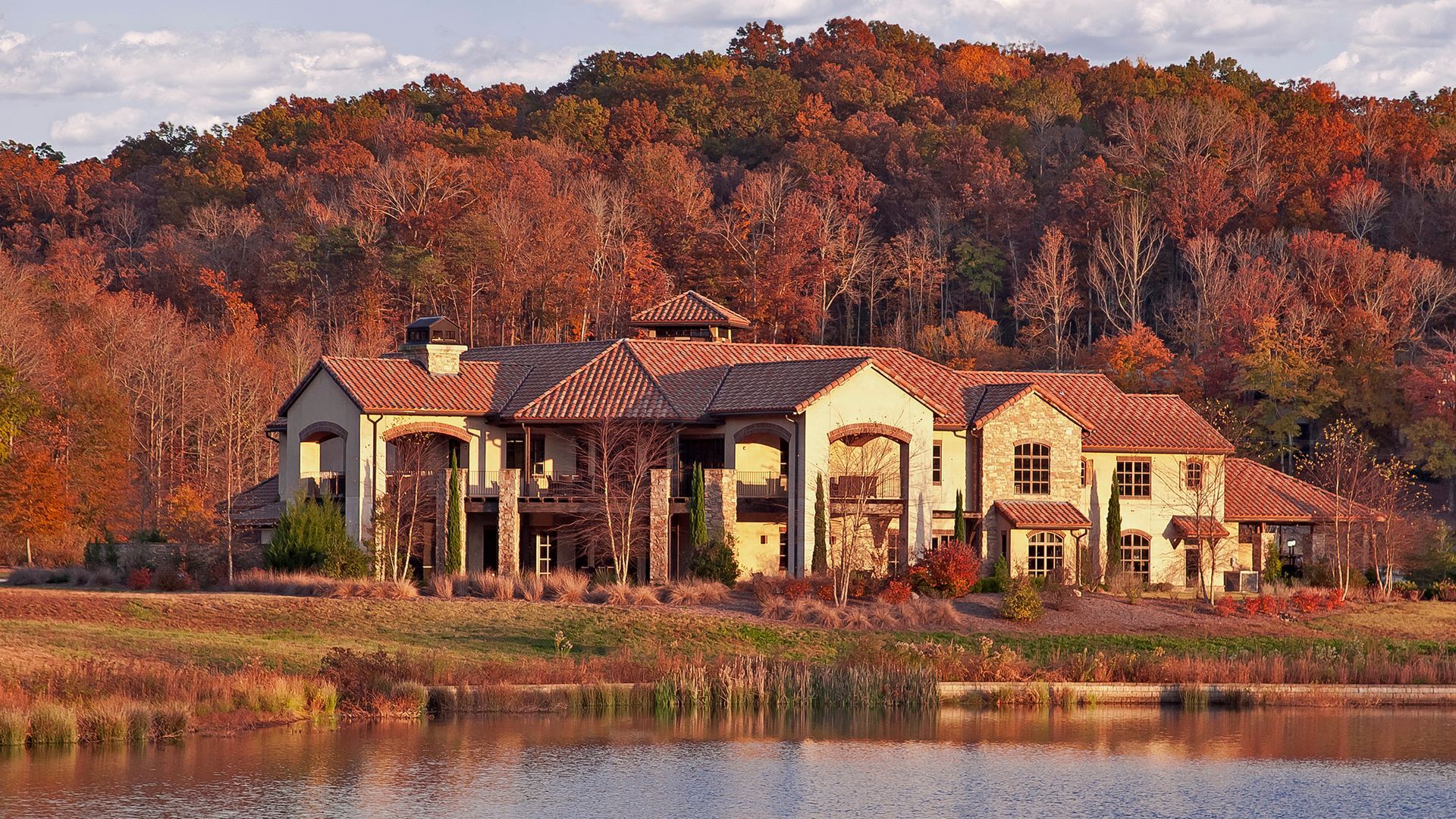 A large house is sitting on the shore of a lake surrounded by trees.