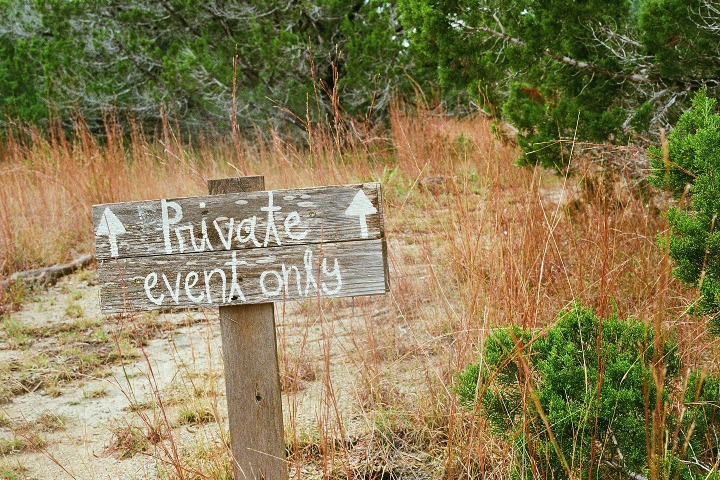 A weathered wooden sign on a post in a grassy field reads 