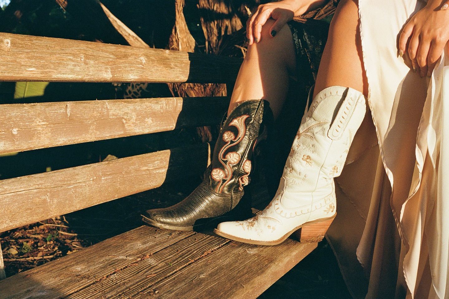 A person wears one black and one white patterned cowboy boot while sitting on a rustic wooden bench.