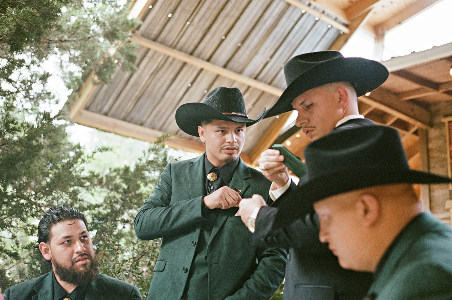 Four men in dark suits and cowboy hats stand together in an outdoor, wooden pavilion setting.
