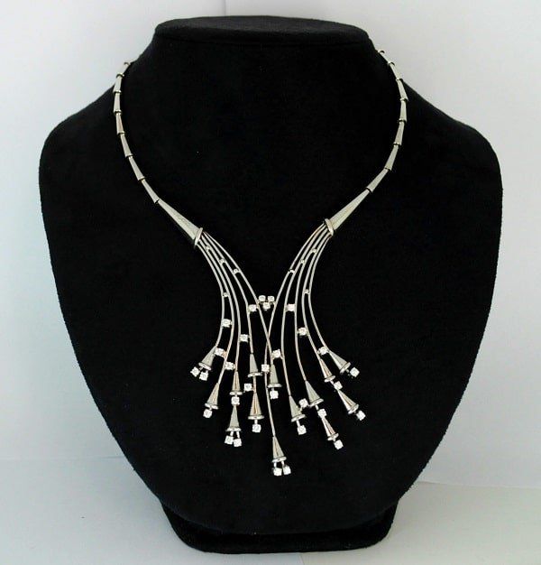 Silver necklace on a black mannequin. It has a V-shaped design with cone-shaped pendants.