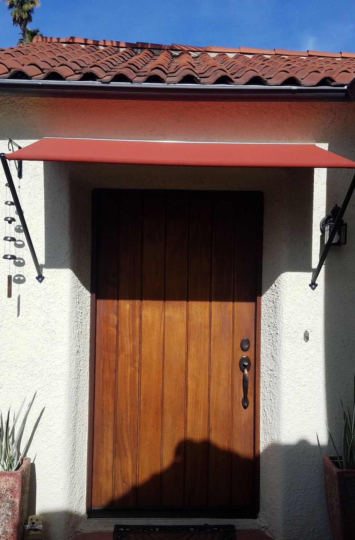 Wooden door under a red awning with support arms.