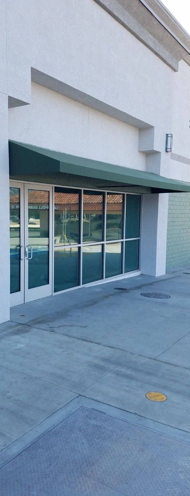 A storefront with a green awning and large glass windows. The exterior is white with a blue-gray concrete path in front.