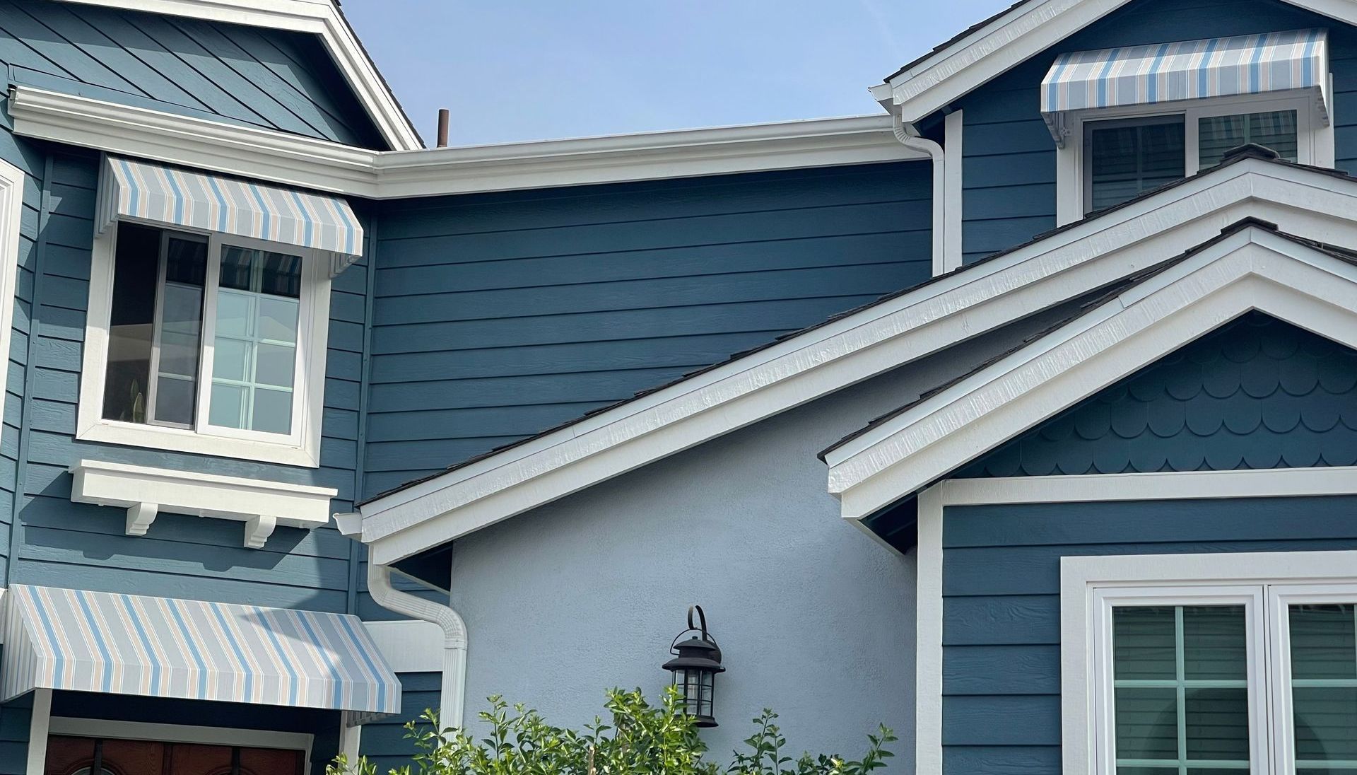 A blue house with white trim and awnings on the windows