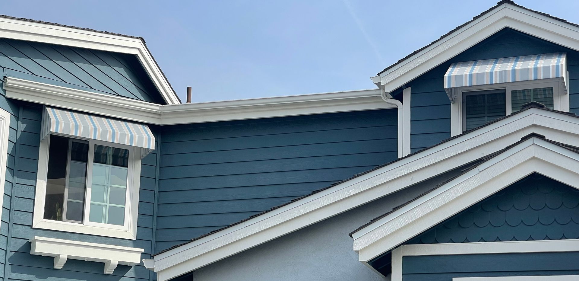 A blue house with white trim and awnings on the windows