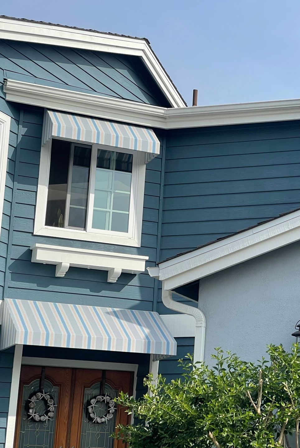 Blue house with striped awnings over windows; a sunny day.