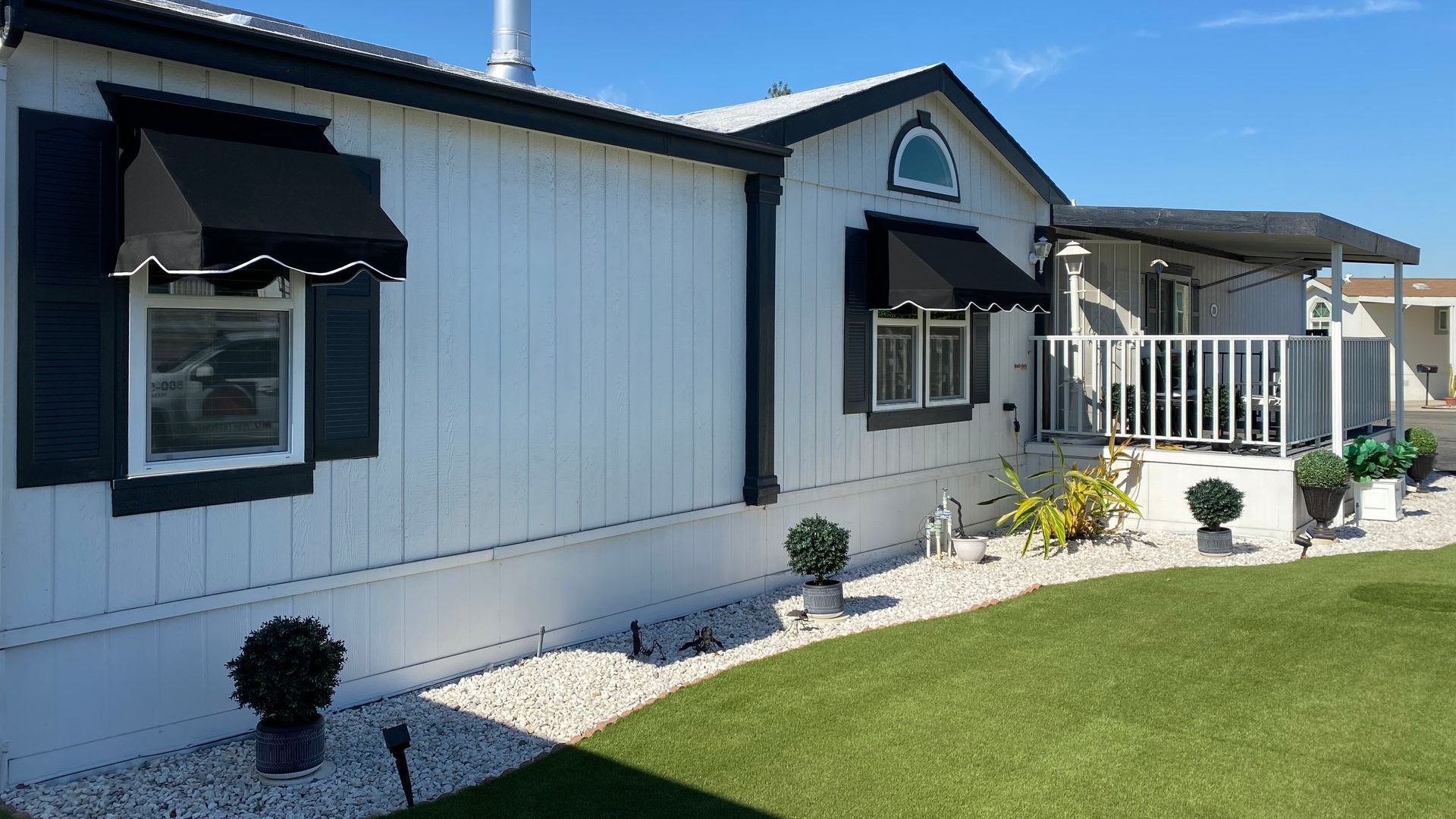 A white mobile home with black shutters and a porch.