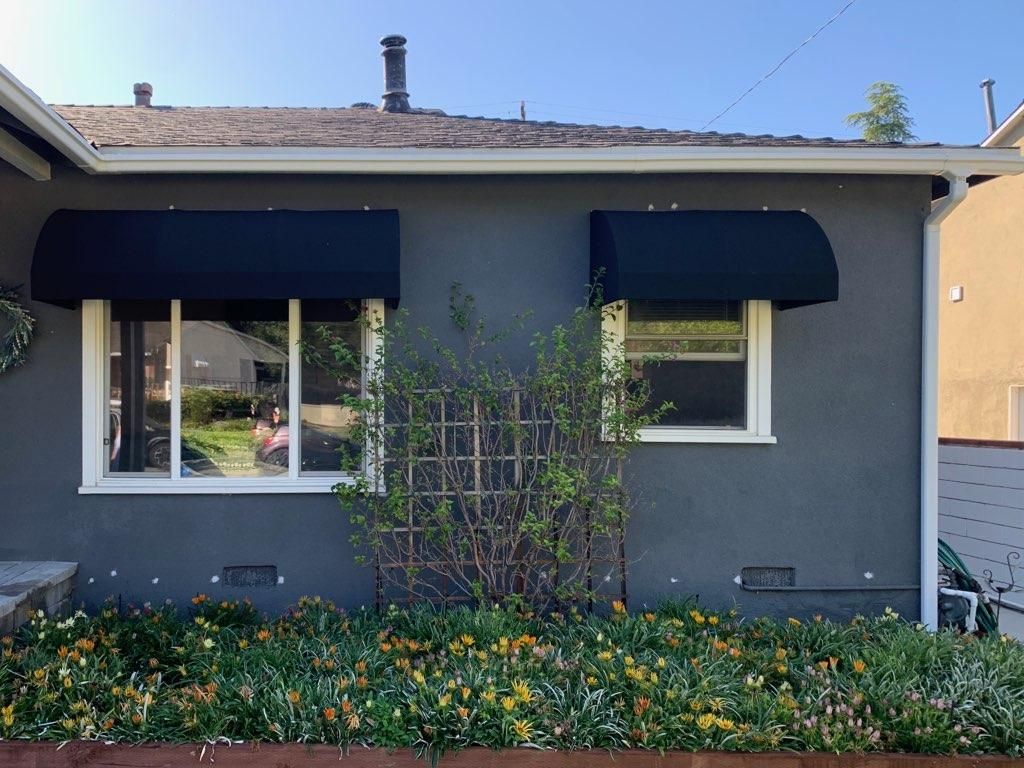 A gray house with black awnings on the windows