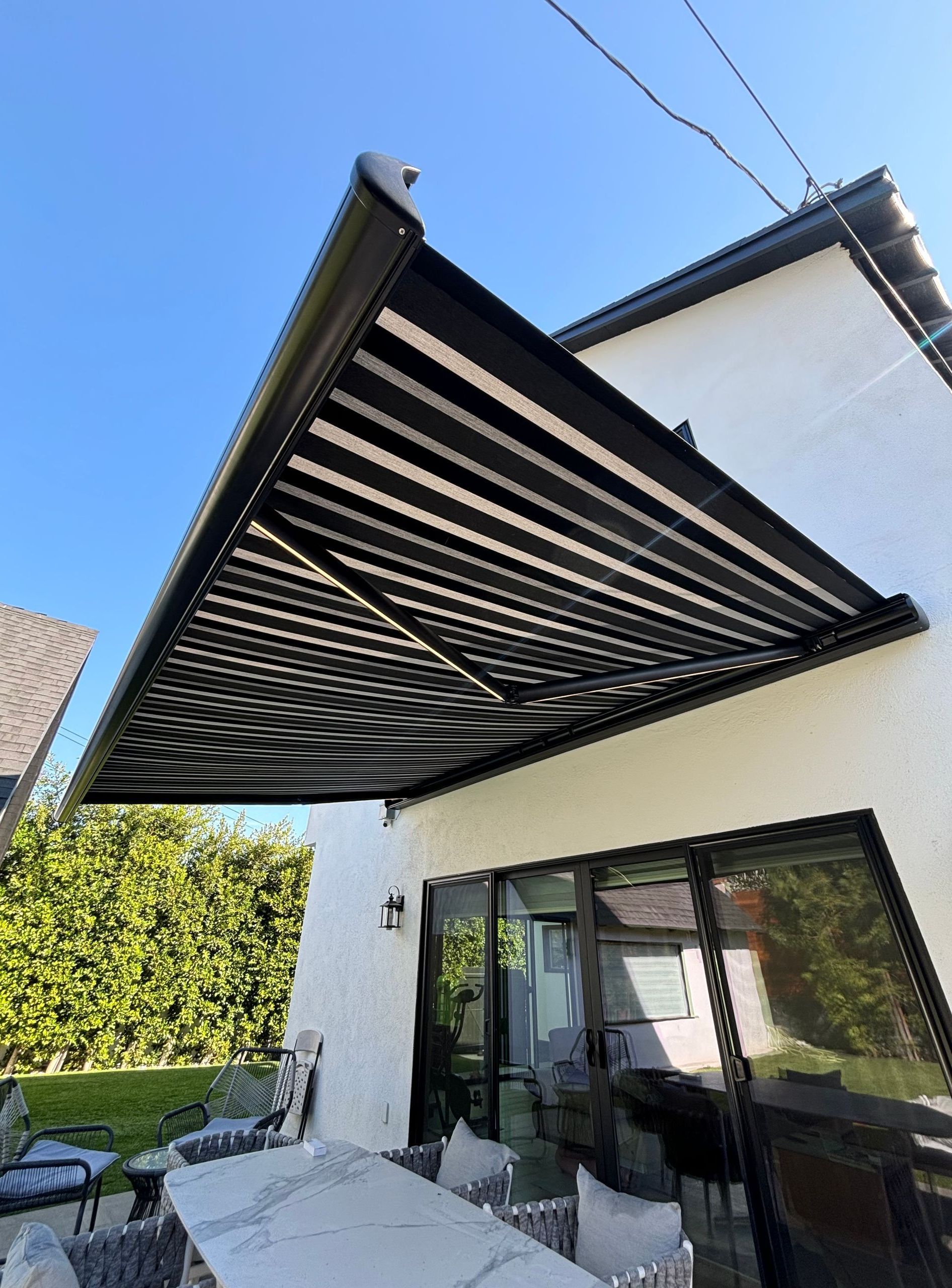 A black awning is covering a patio with a table and chairs underneath it.