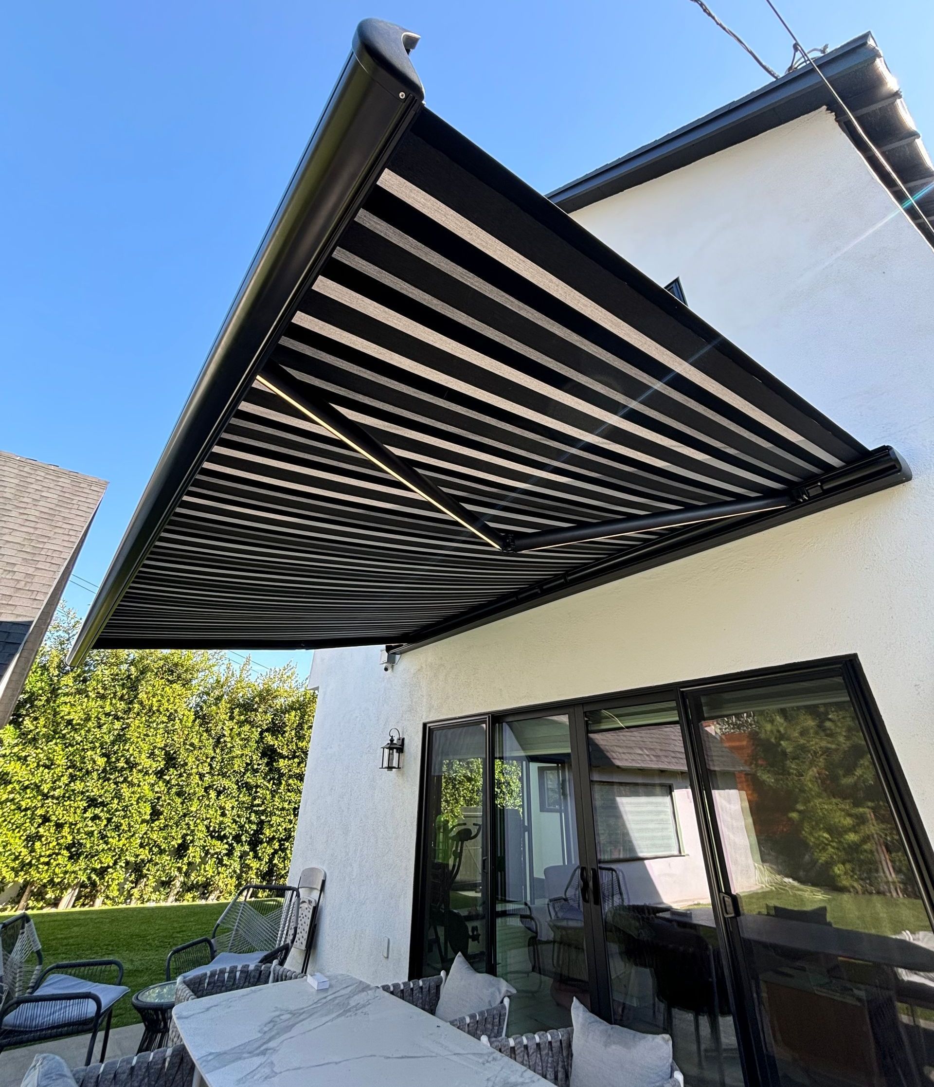 A black awning is covering a patio with a table and chairs.