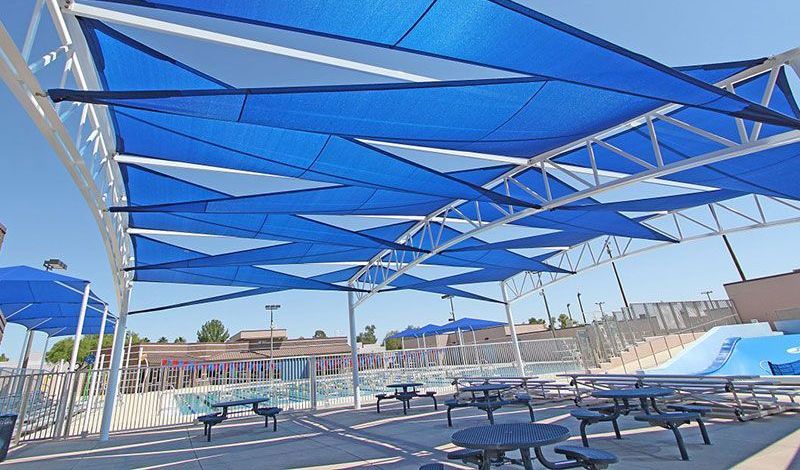 A swimming pool with tables and chairs under blue umbrellas.