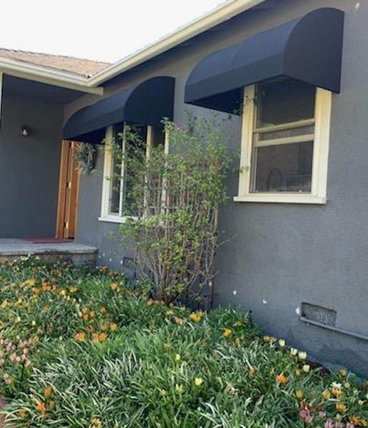 A gray house with black awnings on the windows