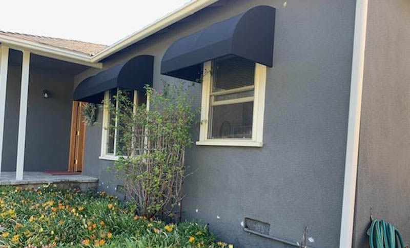 A gray house with a black awning on the windows.