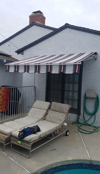 Two lounge chairs under an awning next to a pool.