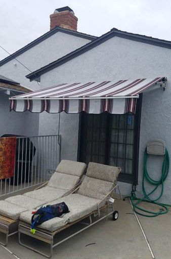 A person is laying on a lounge chair under an awning on a patio.