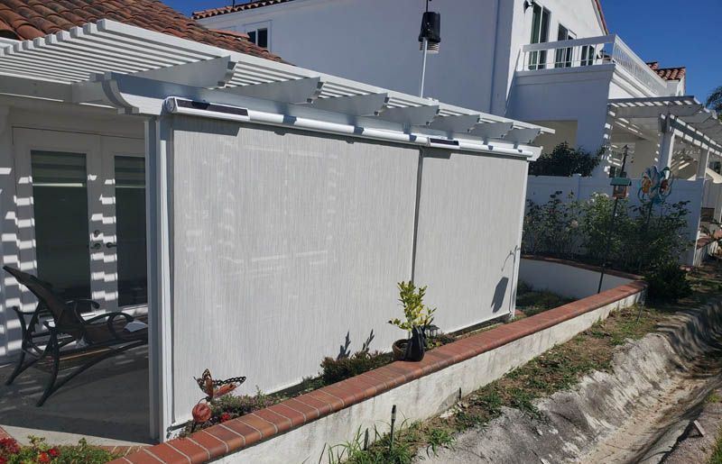 A white house with a pergola and blinds on the side of it.