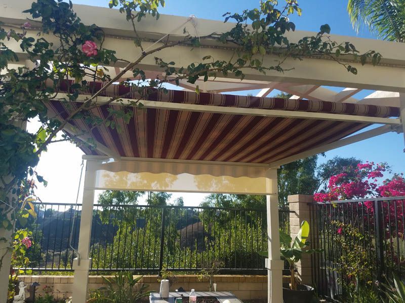 Pergola with retractable red and white striped awning, plants and flowers.
