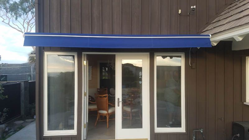 A house with a blue awning over the door and windows.