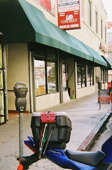 A blue motorcycle is parked in front of a building with a green awning