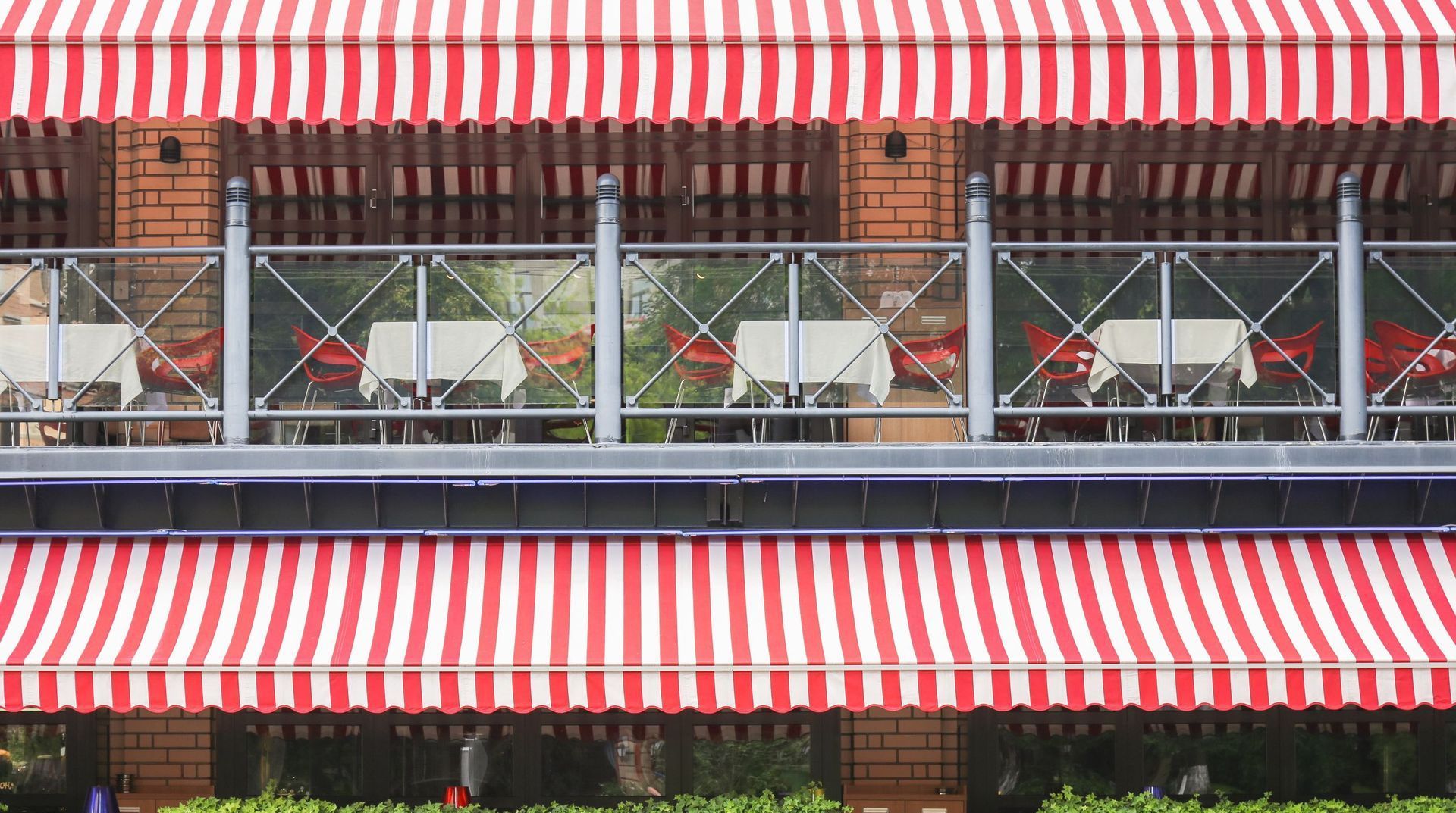 A red and white striped awning over a balcony with tables and chairs.