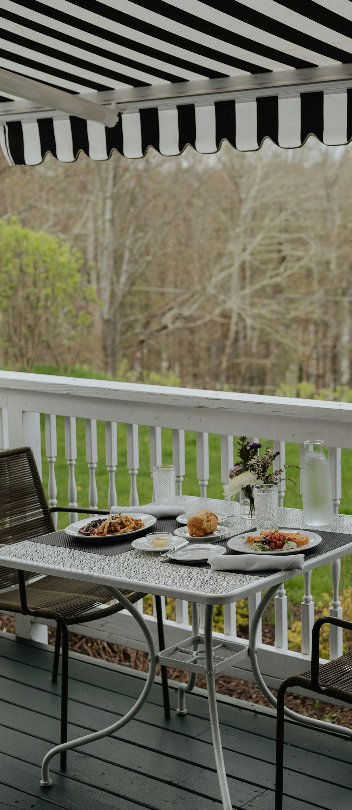 A table and chairs on a deck with a black and white awning.