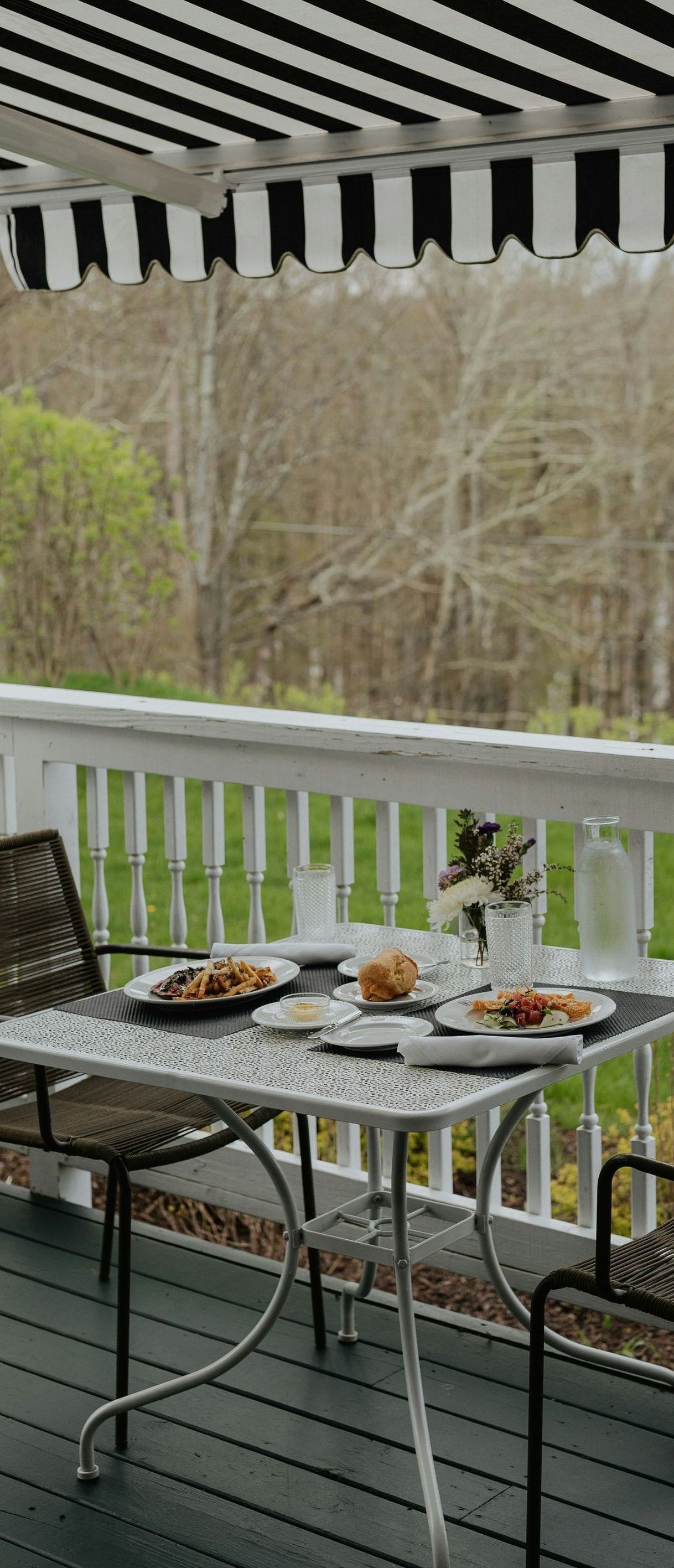 There is a table and chairs on the deck with plates of food on it.