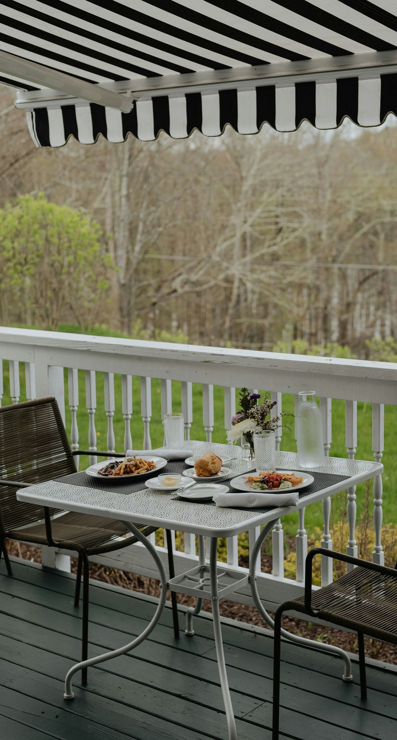 A table and chairs on a deck with a black and white awning.