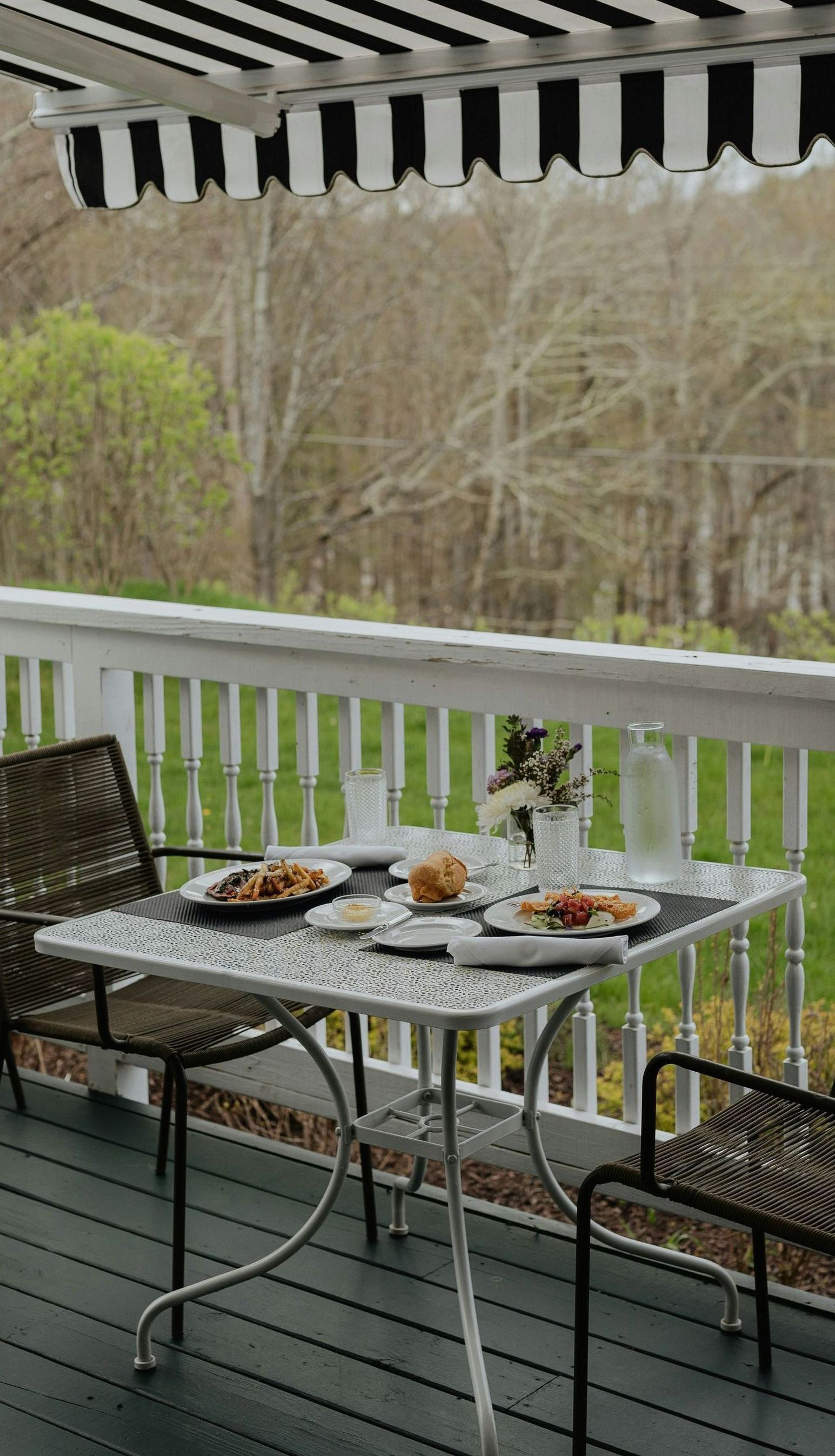 A table with plates of food on it is on a deck with a black and white awning.