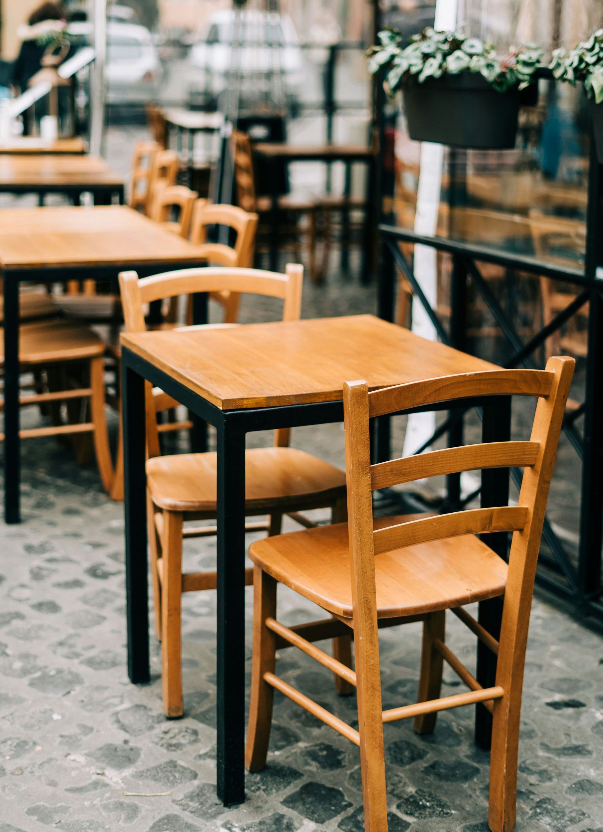 A row of wooden tables and chairs outside of a restaurant.