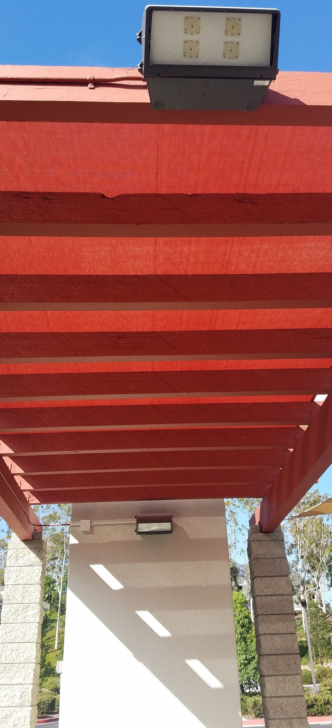 Red pergola roof with a spotlight, over a white support beam.